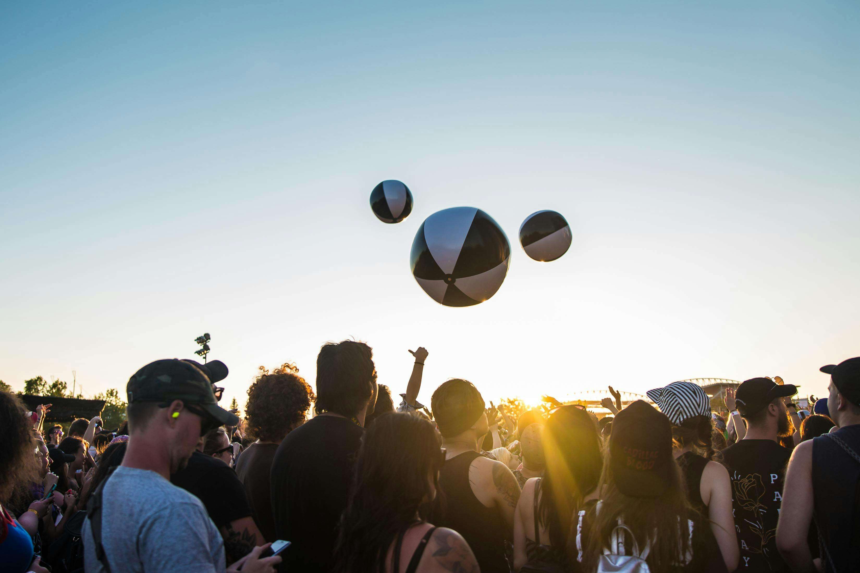 Lively crowd enjoying a music festival outdoors at sunset with beach balls bouncing in the air.