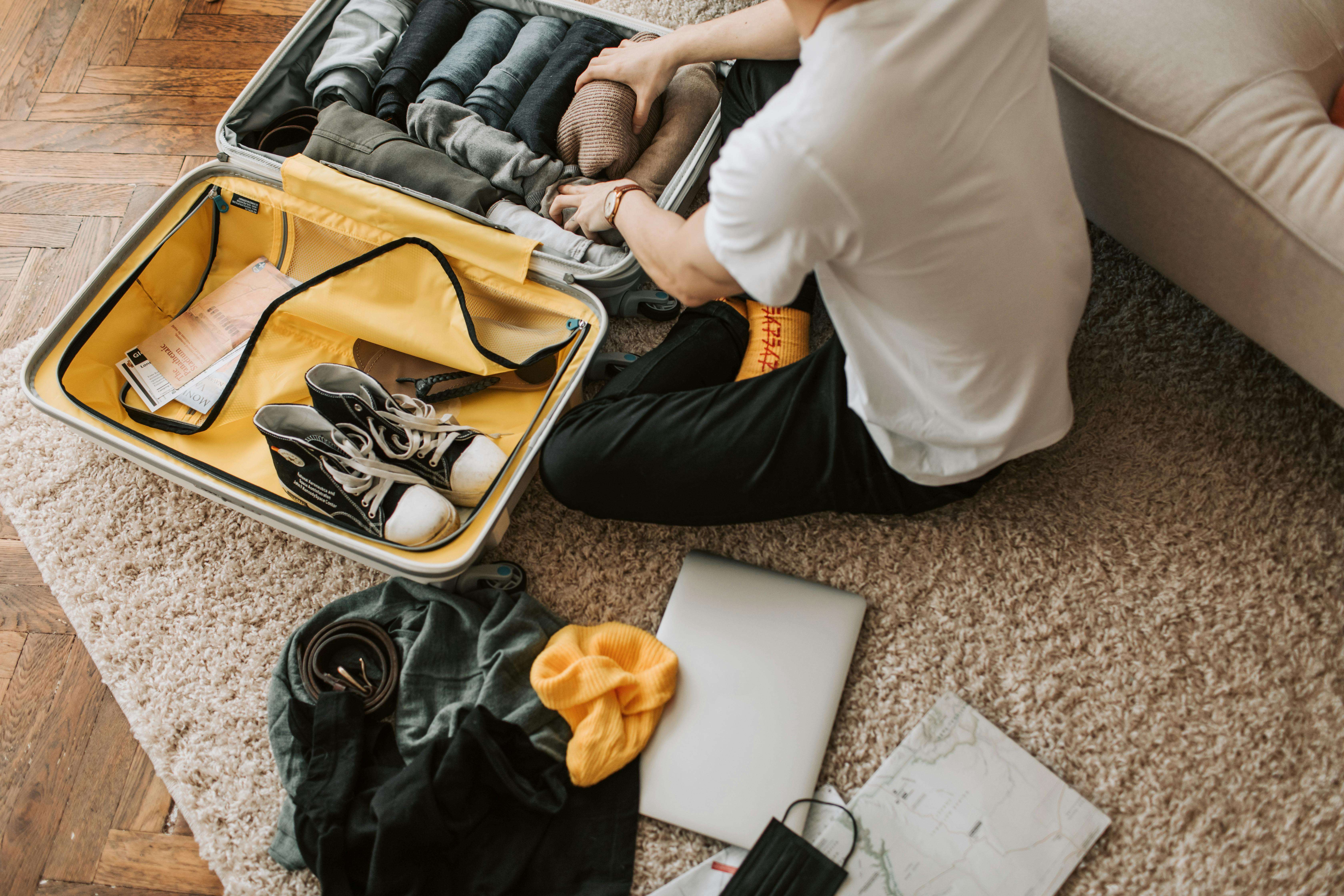 Man organizing clothes and essentials into a yellow suitcase for travel in a cozy living room.